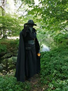 a man dressed as darth vader standing in the woods with his hat on