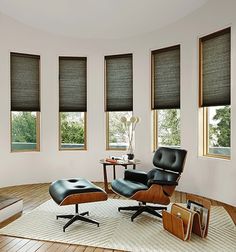 a living room with three windows and a chair in the middle on a rug next to a coffee table