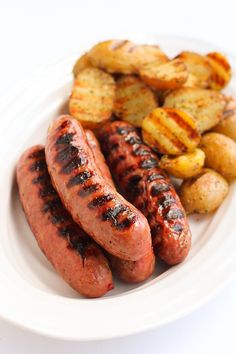 two sausages and potatoes on a plate next to potato wedges in a bowl