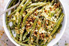 a white bowl filled with green beans covered in cheese and seasoning next to a spoon