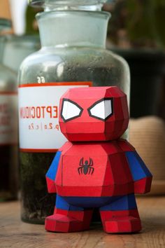 a spider man paper toy sitting on top of a wooden table next to a jar