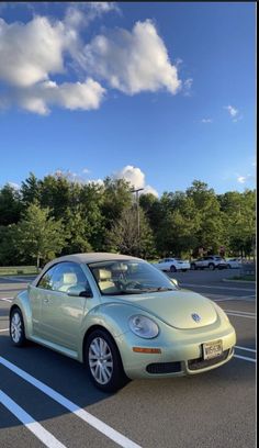 a green car parked in a parking lot next to some trees and clouds on a sunny day