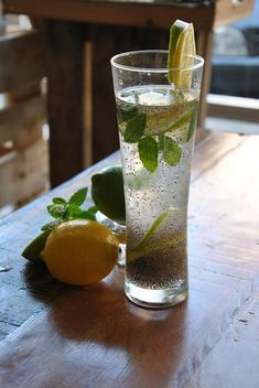 a glass filled with water sitting on top of a table next to lemons and mint