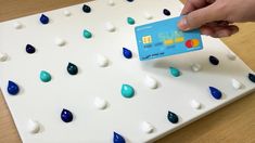 a hand is holding a credit card over a white board with blue and green drops