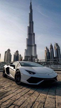 a white sports car parked in front of the burj dubai skyline with skyscrapers