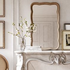 a vase with flowers on top of a mantle next to a mirror and framed pictures