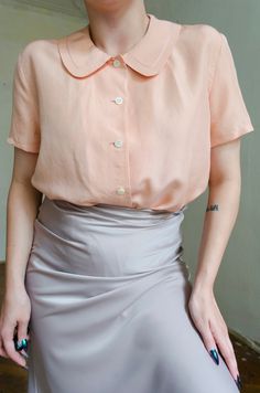 Truly romantic peachy pink silk blouse. Features the cutest Peter Pan collar, button up style and short sleeves. Detailed specs & measurements below: Fabrics: 100% silk Tag size:  1 Brand: Portdimare Best fits: XS - S Condition: superb, no flaws to note MEASUREMENTS *taken seam to seam. not doubled, taken flat Shoulders: 41 cm |  16.1" Bust: 52 cm | 20.4" Sleeve length: 19 cm | 7.4" Length: 67 cm | 26.3" For reference, our model is size S and is 5"2 tall  SHIPPING Sent as Latvian Standard Post. Chic Short Sleeve Peach Blouse, Elegant Short Sleeve Pink Blouse, Elegant Pink Short Sleeve Blouse, Vintage Pink Blouse With Peter Pan Collar, Feminine Pink Collared Top, Pink Short Sleeve Feminine Blouse, Classic Pink Summer Blouse, Pink Silk Blouse, Pastel Blouse