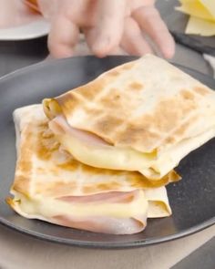 two quesadillas sitting on top of a black plate next to a person's hand