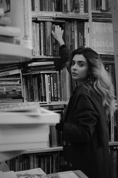 a woman standing in front of a bookshelf with her hand on the book shelf