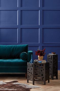 a living room with blue walls and wooden flooring is pictured in this image, there are two end tables next to the couch