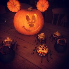 a mickey mouse pumpkin sitting on top of a wooden table next to cupcakes