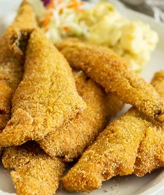 some fried food on a white plate with coleslaw and mashed potatoes in the background