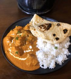 a black plate topped with rice and curry next to a tortilla covered in sauce