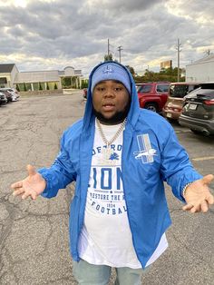 a man standing in a parking lot with his hands out and wearing a blue jacket