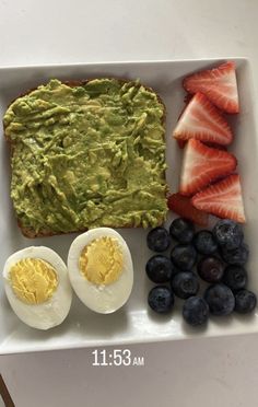 a white plate topped with eggs, fruit and an avocado spread next to sliced strawberries