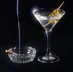 two martini glasses with olives in them on a black background, one is half filled and the other half empty