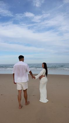 a man and woman holding hands on the beach