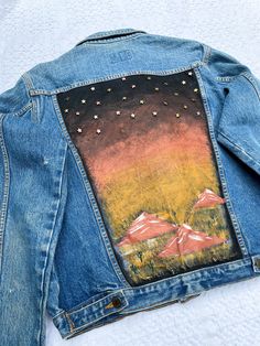 a jean jacket with an image of mountains painted on the back and gold stars in the sky