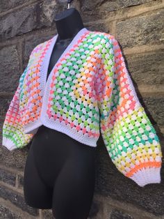 a mannequin wearing a multicolored crochet jacket on top of a brick wall