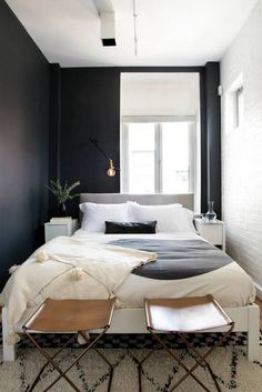 a bedroom with black walls, white bedding and two stools in front of the bed