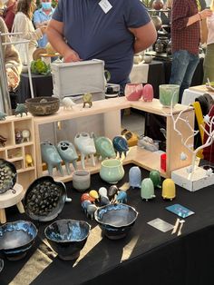 a man standing next to a table with bowls and plates on it at an outdoor market