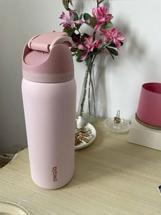 a pink cup sitting on top of a wooden table next to a vase with flowers