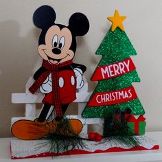 a mickey mouse standing next to a christmas tree with a merry sign on it's side