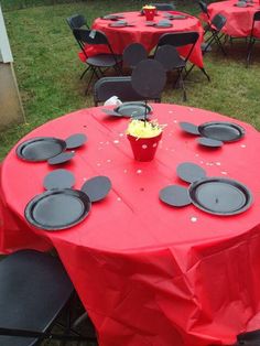 a red table with black plates and mickey mouse napkins on it in the grass