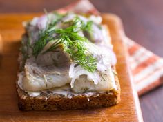 a piece of bread topped with fish and dill on top of a wooden cutting board