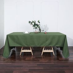 a green table cloth on top of a wooden table with two white plates and flowers