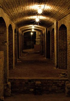 an empty tunnel with brick walls and arches on either side is lit by a light bulb