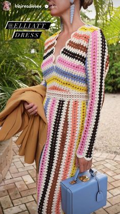 a woman in a multicolored crochet dress holding a blue purse