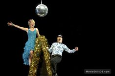 a man and woman are dancing on stage with a disco ball hanging from the ceiling