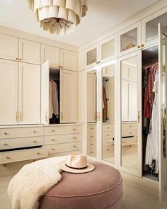 a dressing room with white closets and an ottoman in front of the wardrobe door