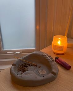 a table with a candle, bowl and paintbrush on it next to a window