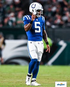 a football player standing on the field with his hand up to his ear and wearing a helmet