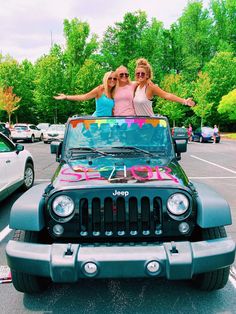 two women standing on top of a jeep in a parking lot