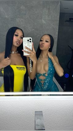 two beautiful women standing in front of a mirror taking a selfie with their cell phone