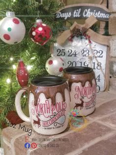 two coffee mugs sitting next to a christmas tree