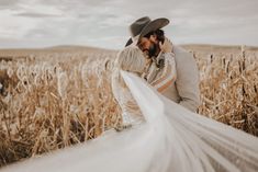 a bride and groom standing in a wheat field