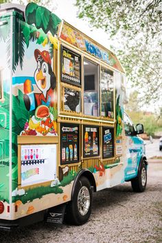 a brightly colored food truck is parked on the side of the road in front of a tree