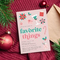 a pink christmas card sitting on top of a red blanket next to ornaments and envelope