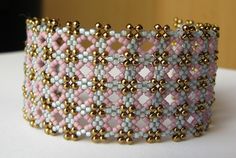 a pink and white beaded bracelet with gold beads on it's sides, sitting on a table