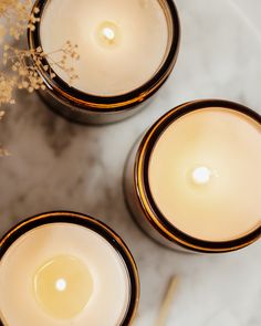 three lit candles sitting on top of a white marble table next to some dried flowers