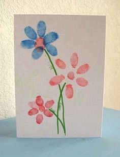 a card with watercolor flowers on it sitting on a blue tablecloth next to a white wall