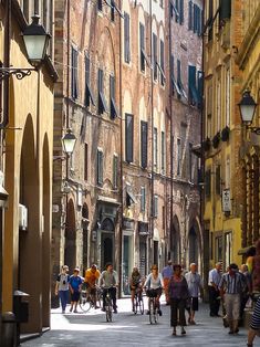 many people are walking and riding bicycles down the street in an old european city with tall buildings