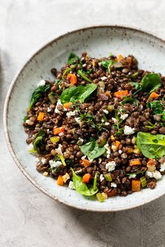 a white bowl filled with lentils and spinach on top of a marble table