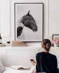 a woman sitting on a bed holding a glass of wine in front of a horse print