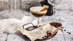 two glasses filled with drinks sitting on top of a table next to papers and coffee beans