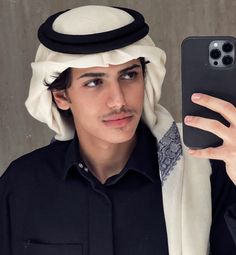 a man holding up a cell phone in front of his face while wearing a headscarf